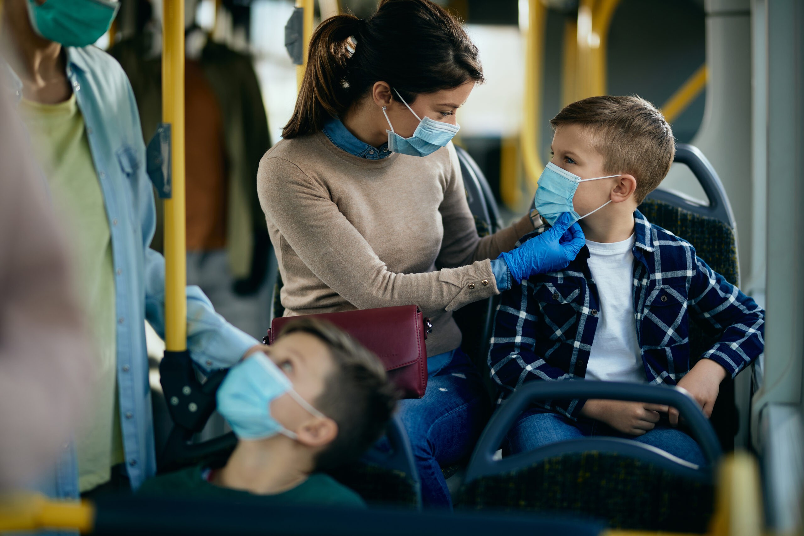 Caring mother adjusting son's protective face mask while commuting by public transportation.